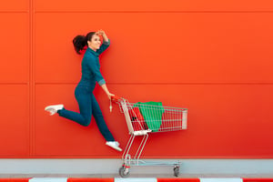 woman with shopping cart leaping into the air in front of red background